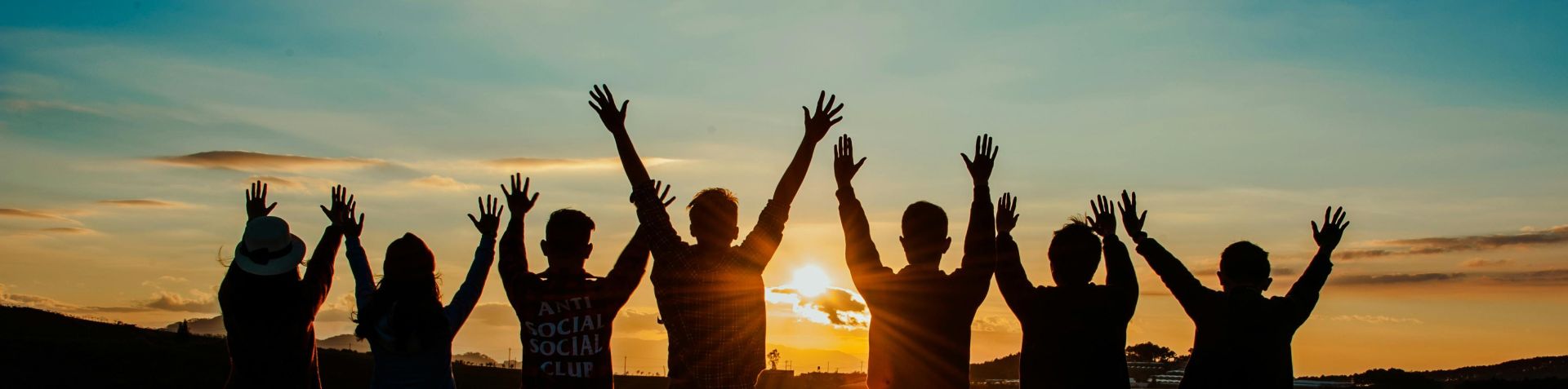 A diverse group of friends raises their arms in celebration against a vibrant sunset backdrop.