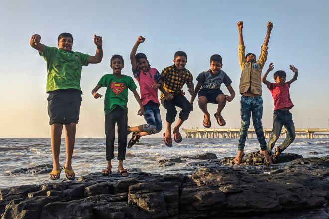 Group of kids joyfully jumping on rocks by the seaside. Fun and playful moment captured outdoors.